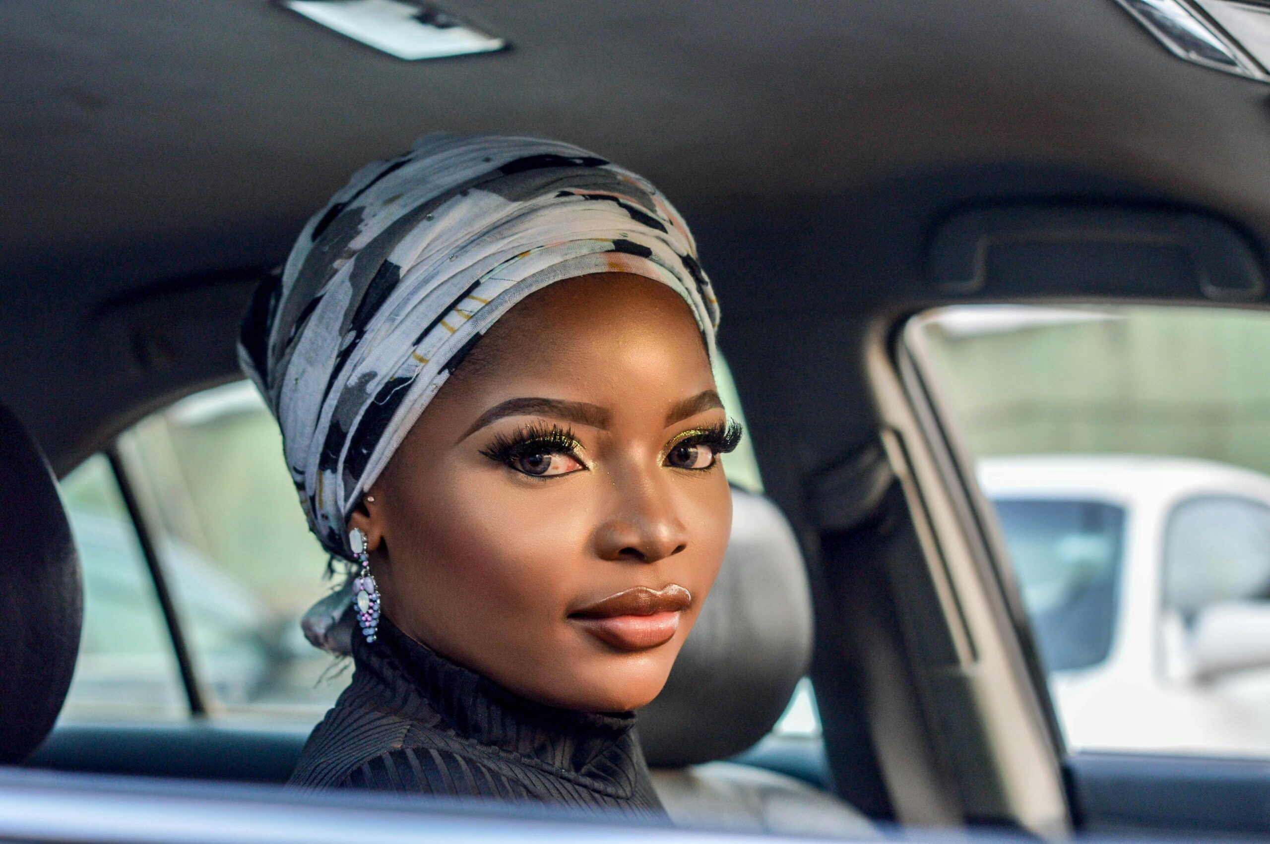 Portrait of a beautiful woman wearing a headscarf sitting inside a car, showcasing elegance and beauty.